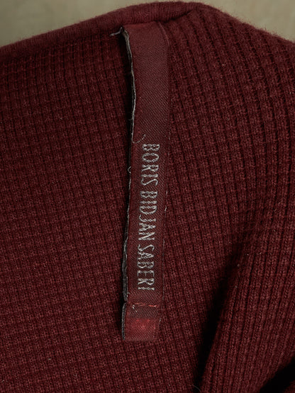 Close-up of a ribbed burgundy knit garment with a vertical fabric label reading 'BORIS BUDJAN SBERI'.