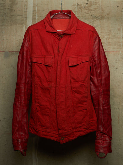 A red jacket with a matte textured body and glossy leather sleeves, hanging on a wire hanger against a concrete wall.