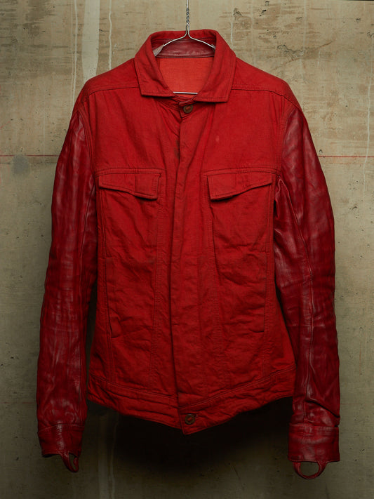 A red jacket with a matte textured body and glossy leather sleeves, hanging on a wire hanger against a concrete wall.