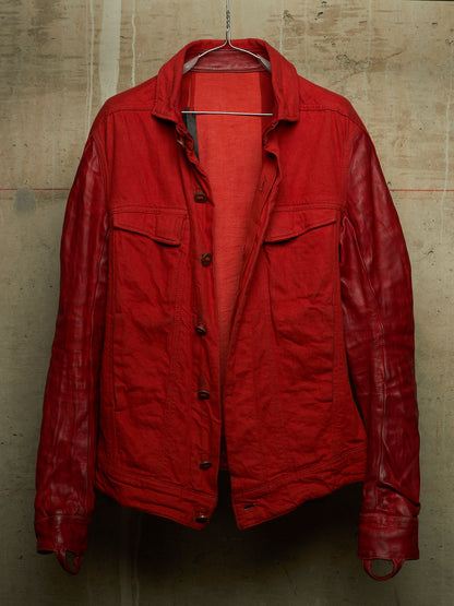 A red jacket with a matte cotton body and glossy leather sleeves, hanging on a wire hanger against a textured concrete wall.
