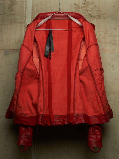 A red hooded jacket with integrated red gloves, hanging on a metal hanger against a textured concrete wall.