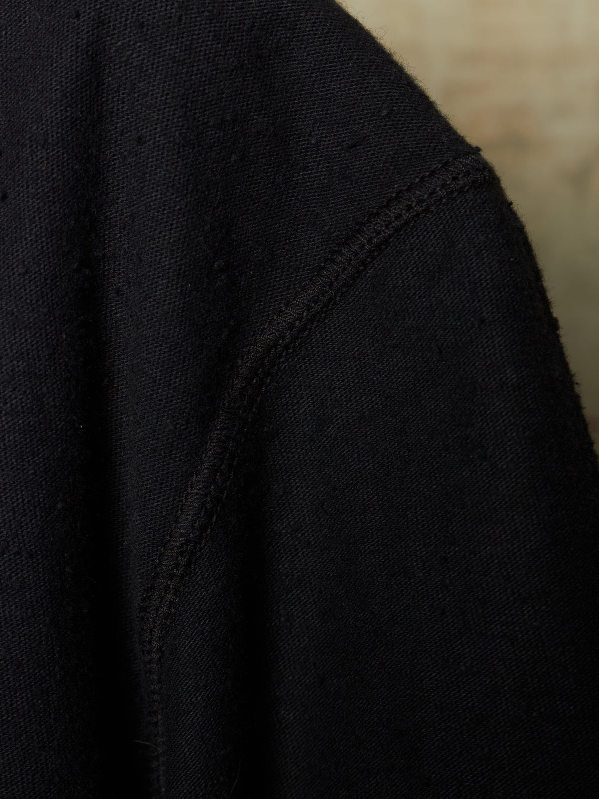 Close-up detail of a black knit garment, showing the texture of the fabric and a seam against a neutral beige background.
