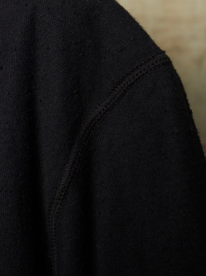Close-up detail of a black knit garment, showing the texture of the fabric and a seam against a neutral beige background.