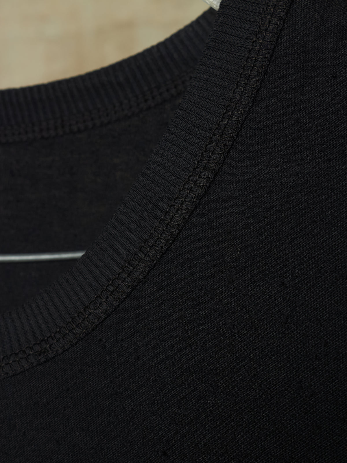 Close-up detail of a black knit garment showing the ribbed crew neck collar and fine fabric texture.