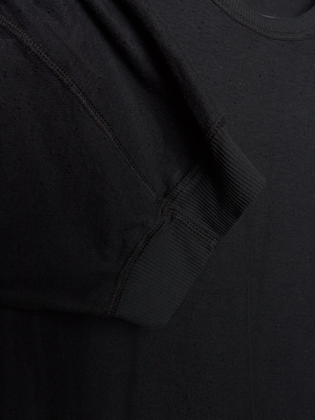 Close-up detail of a black crewneck sweatshirt showing the ribbed sleeve cuff and textured fabric.
