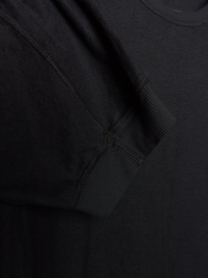 Close-up detail of a black crewneck sweatshirt showing the ribbed sleeve cuff and textured fabric.