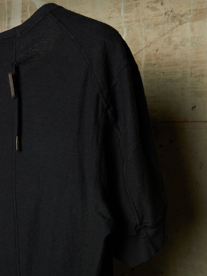A close-up of a black textured knit top or sweater sleeve and shoulder, hanging against a warm beige concrete wall.