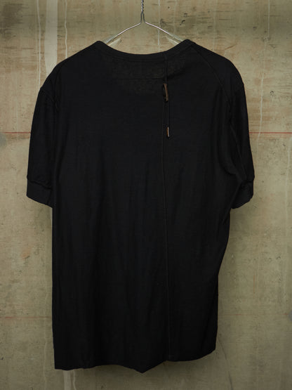 A black short-sleeve top hanging on a metal hanger against a textured concrete wall. The shirt features a unique front zipper closure with small brown pull tabs and a sheer mesh yoke at the neckline.