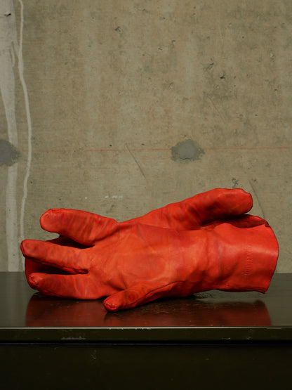 A pair of bright red leather gloves resting on a dark reflective surface against a textured concrete wall.