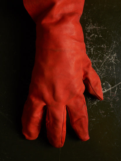 A single long red leather glove laid flat on a dark textured surface.