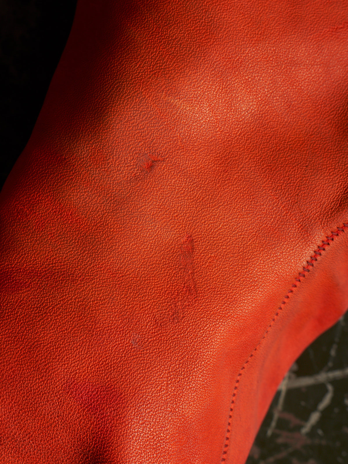 A close-up of a textured red leather surface with visible scuffs and scratches, showing the grain and stitching detail.