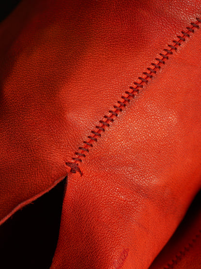 Close-up of textured red leather with a diagonal double-stitched seam and a small tear visible along the edge.