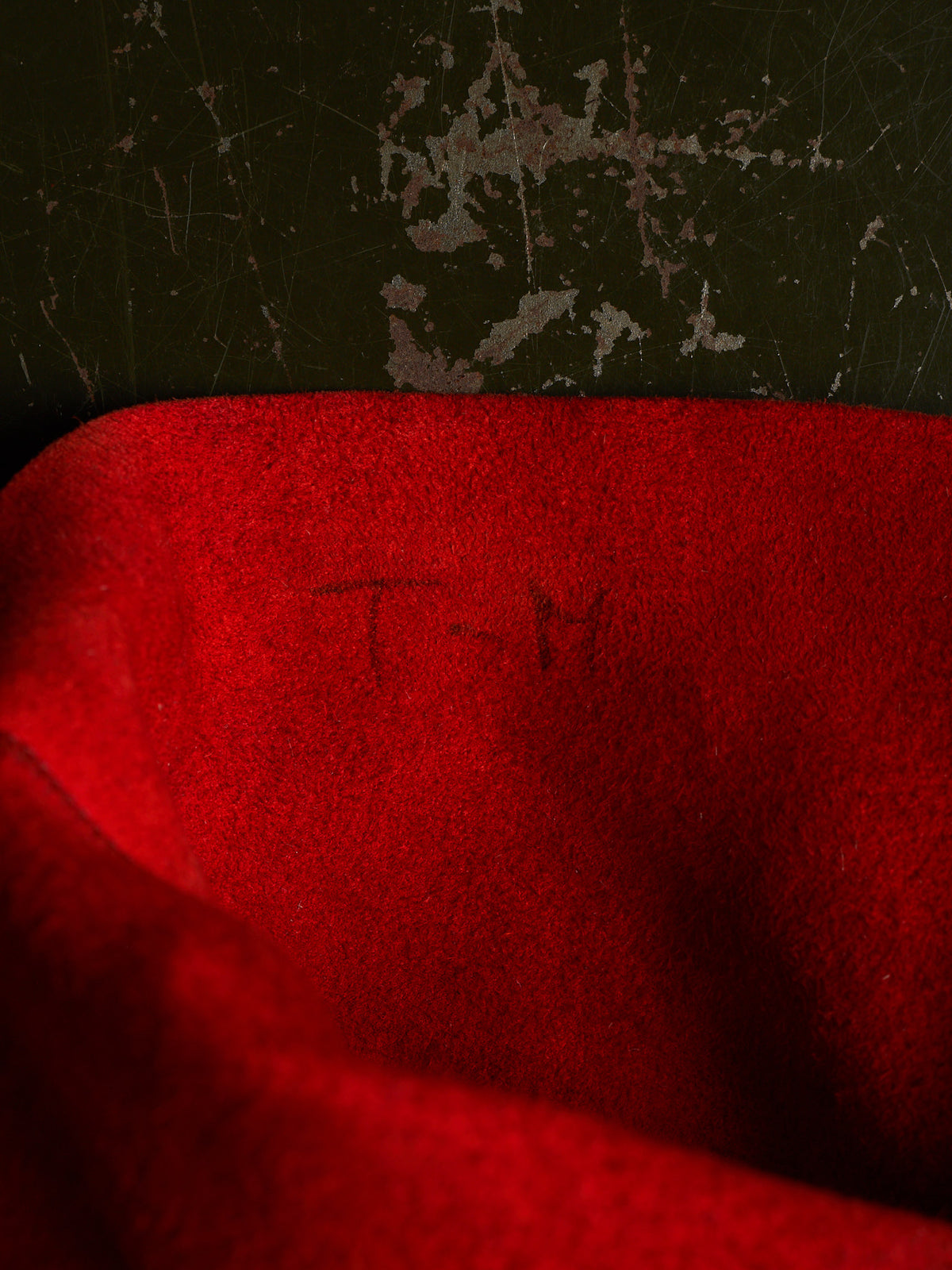 A close-up of a bright red textured fabric surface with faint dark lettering, set against a dark distressed background.