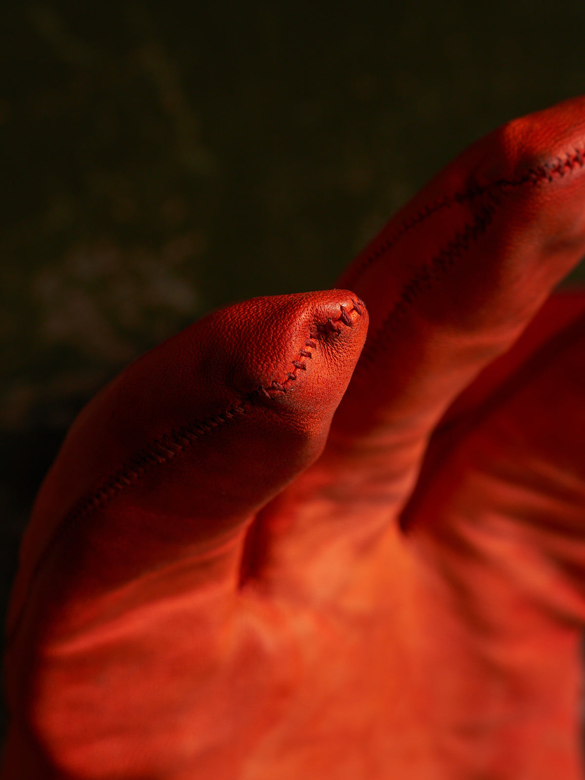 A close-up of a red leather glove with visible stitching, shown against a dark, moody background.