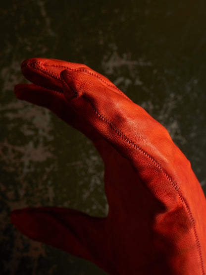 A close-up of a hand wearing a bright red leather glove, set against a dark, textured green background.