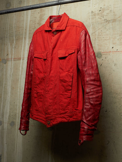 A red jacket with a matte red body and glossy red sleeves, hanging on a metal hanger against a textured concrete wall.