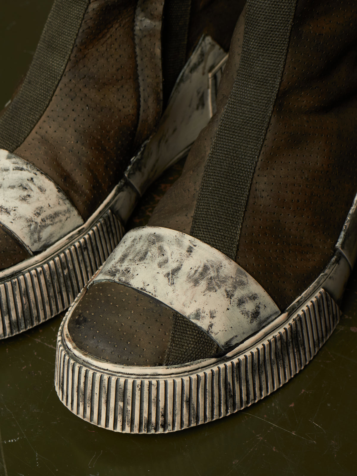 A close-up of a pair of distressed platform sneakers with dark brown suede-like uppers, white canvas toe sections with black scuffing, and thick ribbed black-and-white platform soles.