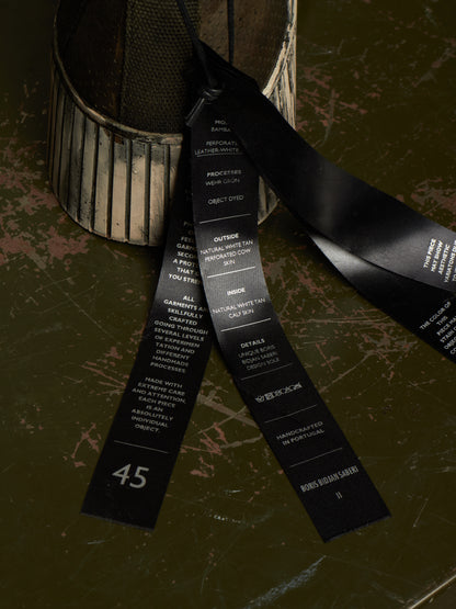 A black fabric ribbon with printed white text details and the number 45, draped over a distressed dark green surface next to a ribbed metal container.