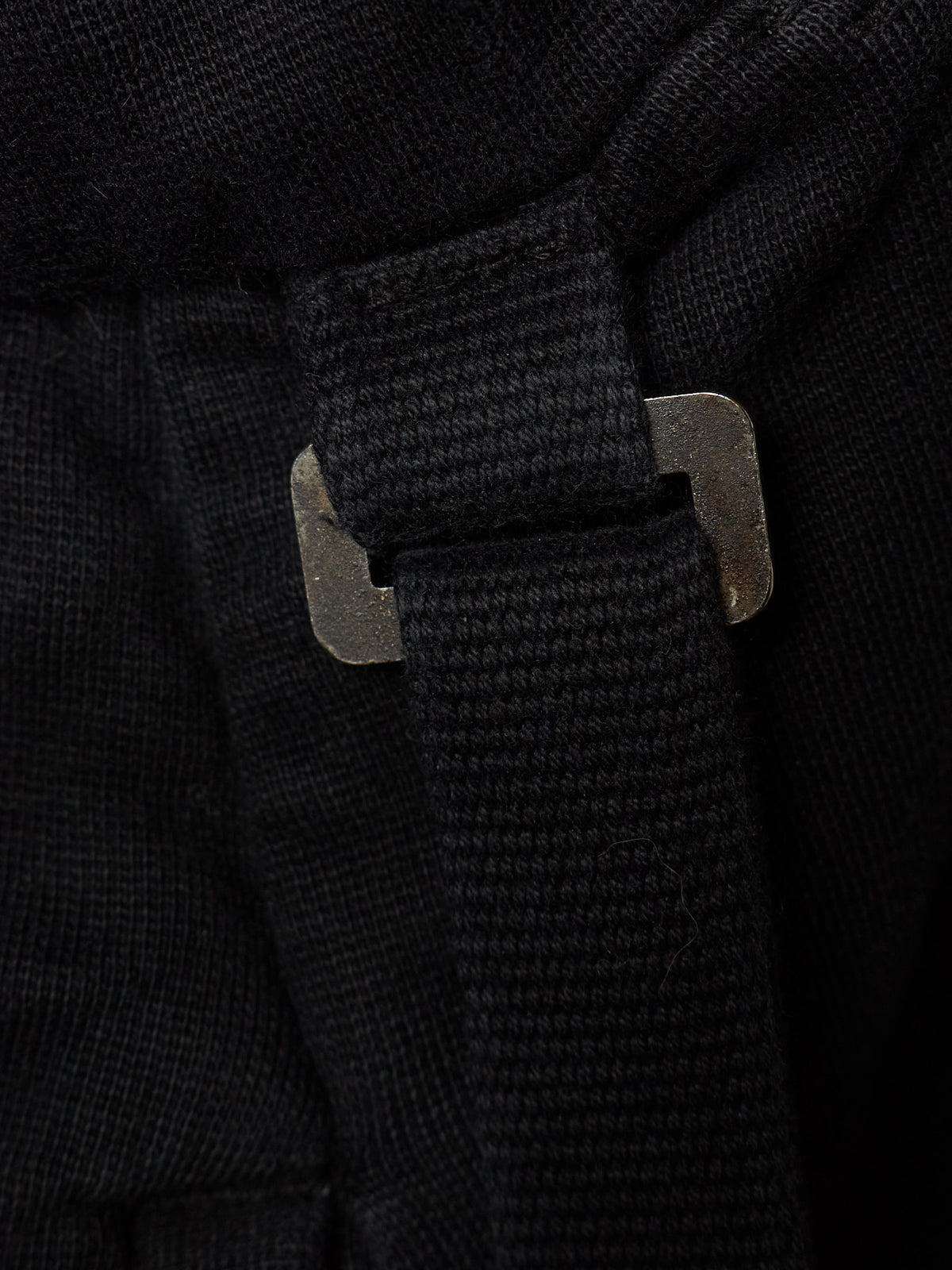 Close-up detail of a black textured fabric item with a black webbed strap and a dark metal buckle.