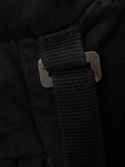 Close-up detail of a black textured fabric item with a black webbed strap and a dark metal buckle.