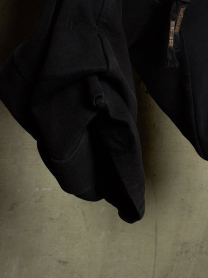A close-up of a black garment, likely a jacket or coat, showing a textured fabric surface and a zipper detail, set against a concrete floor.