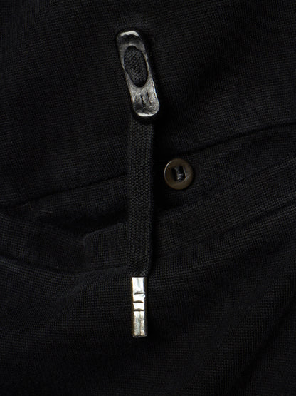 Close-up of a black textured garment showing a silver-toned metal zipper pull, a dark button, and fabric texture.