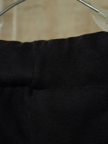 Close-up of a black textured fabric garment, likely a sweater or knit top, hanging on a clear plastic hanger against a beige background.