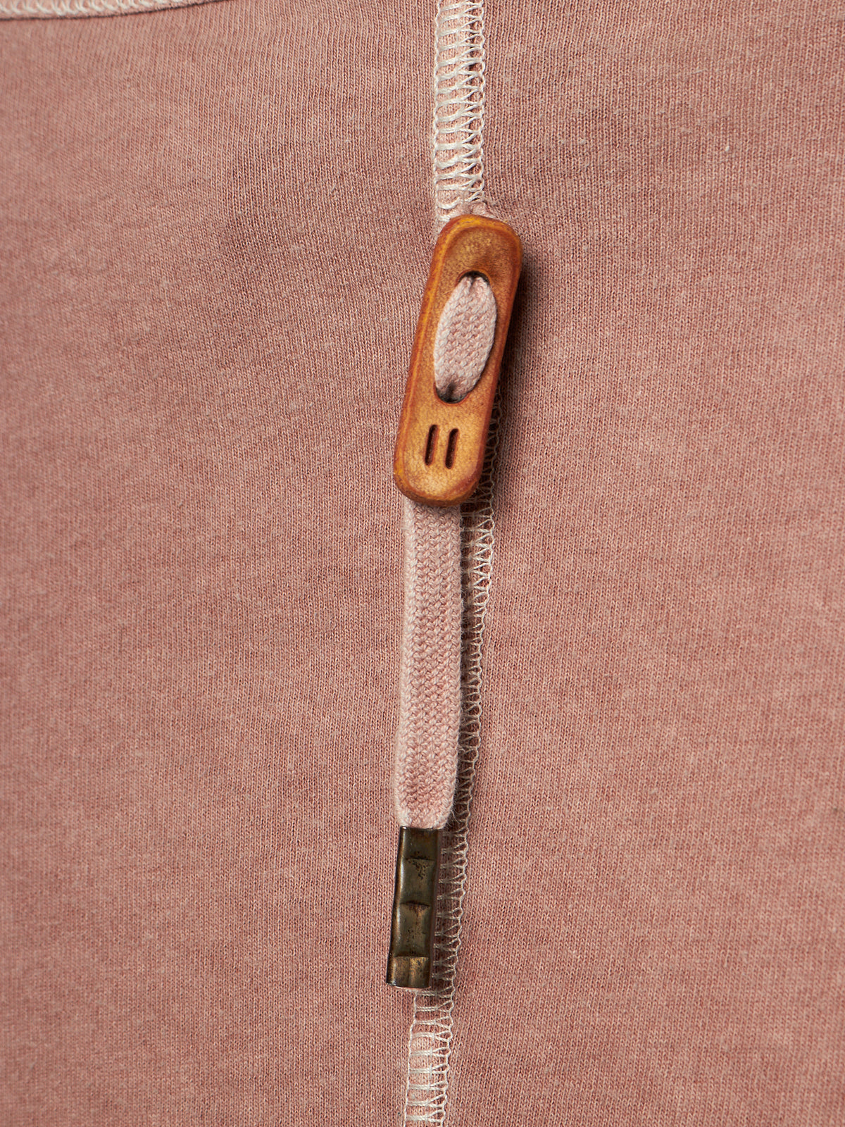 Close-up of a dusty rose pink knit garment featuring a vertical white zipper with a decorative wooden pull tab and a small metallic accent.