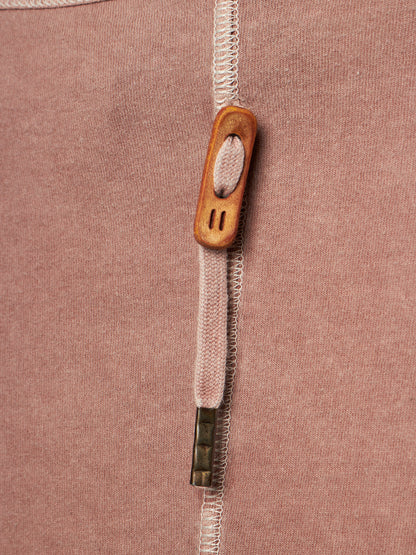 Close-up of a dusty rose pink knit garment featuring a vertical white zipper with a decorative wooden pull tab and a small metallic accent.