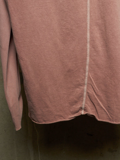 Close-up of a dusty rose pink knit garment, showing a vertical seam and ribbed texture against a dark background.