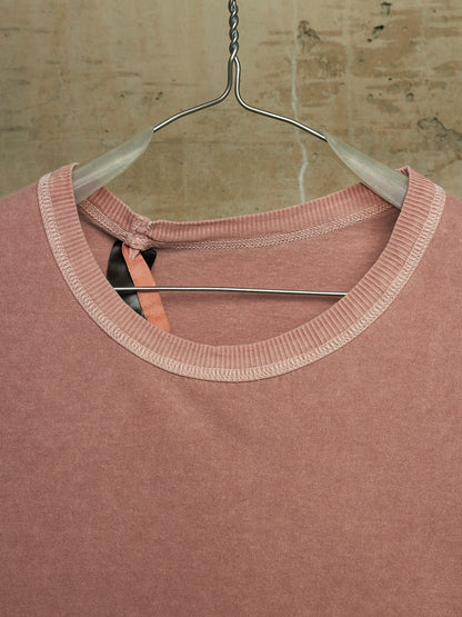 A dusty rose pink knit top with a contrasting light beige ribbed crew neck, hanging on a clear plastic hanger against a textured beige brick wall.