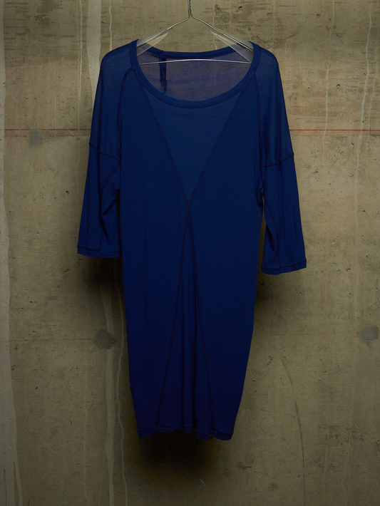 A royal blue sheer mesh dress with three-quarter sleeves and a scoop neckline, hanging on a clear hanger against a textured concrete wall.