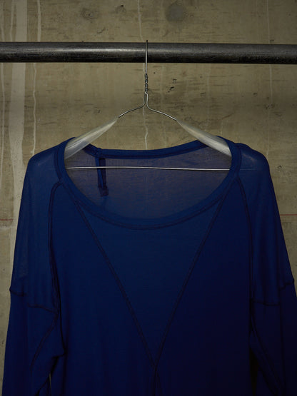 A royal blue sheer long-sleeve top hanging on a white hanger from a metal clothing rack against a textured concrete wall.