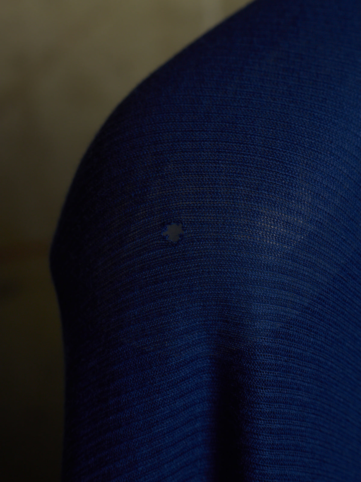 Close-up of a dark blue ribbed knit fabric with a small light-colored star-shaped defect or stain near the center.
