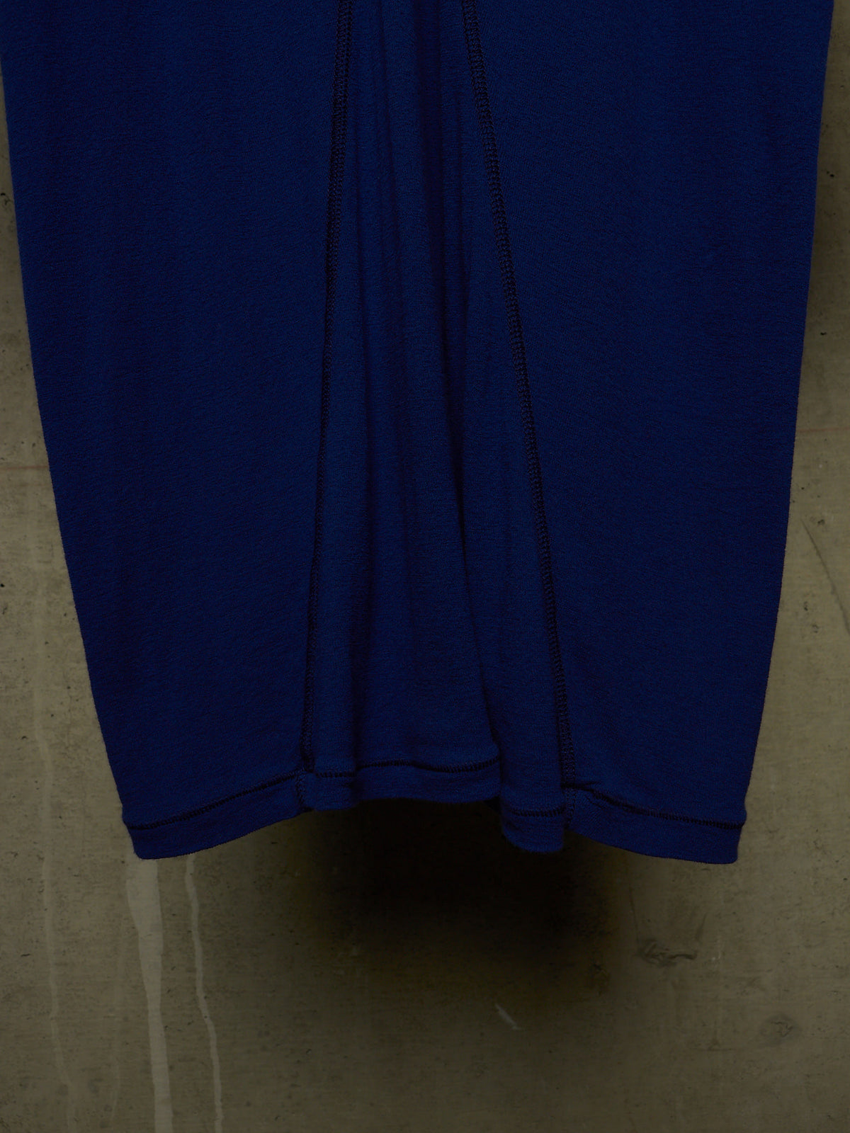 A close-up of a dark blue fabric garment, likely a skirt or dress, showing the hem and vertical seam details against a concrete floor.