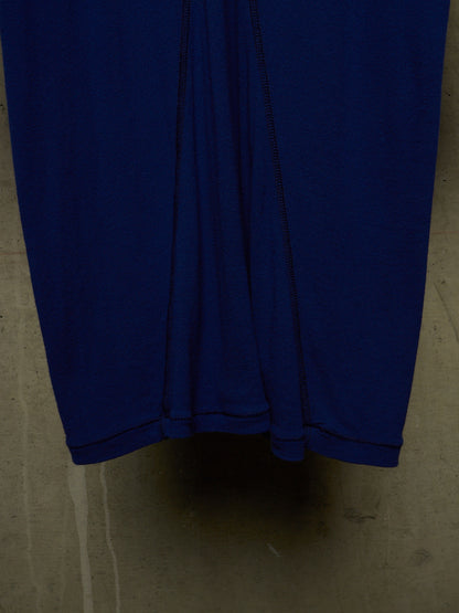 A close-up of a dark blue fabric garment, likely a skirt or dress, showing the hem and vertical seam details against a concrete floor.