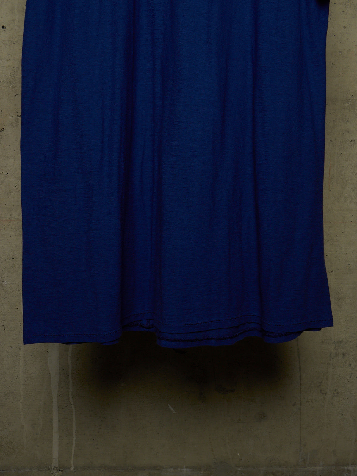 A close-up of a solid dark blue fabric, likely a dress or long skirt, hanging against a textured concrete wall.