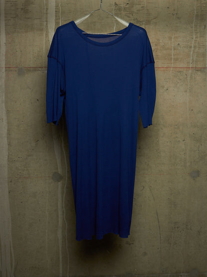 A royal blue long-sleeve dress hanging on a clear plastic hanger against a textured concrete wall.