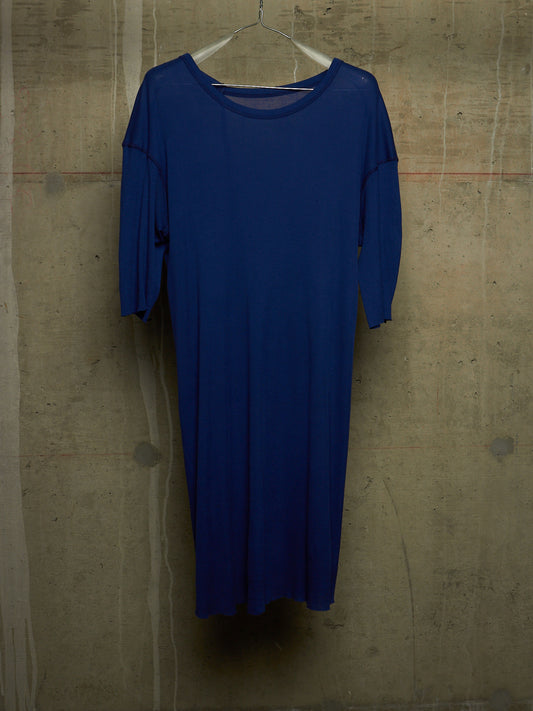 A royal blue long-sleeve dress hanging on a clear plastic hanger against a textured concrete wall.