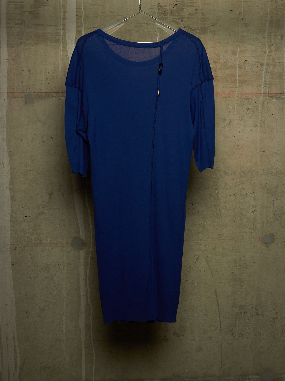 A royal blue midi dress with three-quarter sleeves and a front zipper, hanging on a clear plastic hanger against a textured concrete wall.