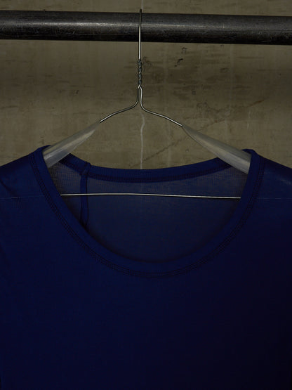 A close-up of a dark blue scoop-neck top hanging on a metal hanger from a dark horizontal bar against a textured concrete wall.