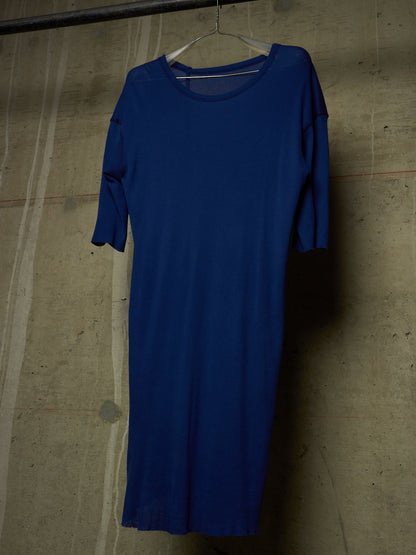 A royal blue short-sleeve dress hanging on a white plastic hanger against a textured concrete wall.