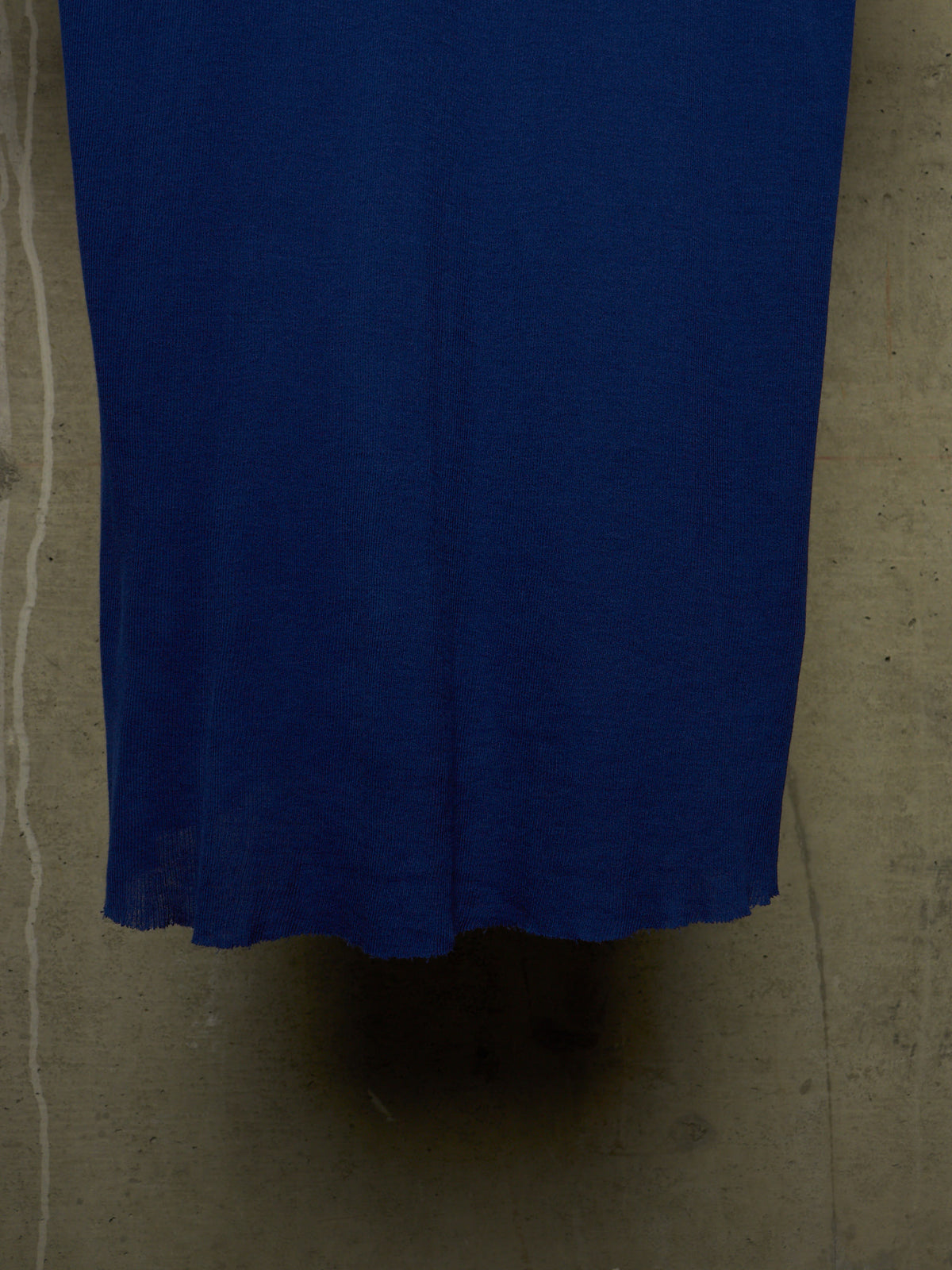 A close-up of a solid royal blue fabric, likely a skirt or dress, hanging against a textured concrete wall.