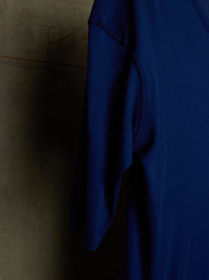 A close-up of a royal blue short-sleeve top hanging against a textured concrete wall.