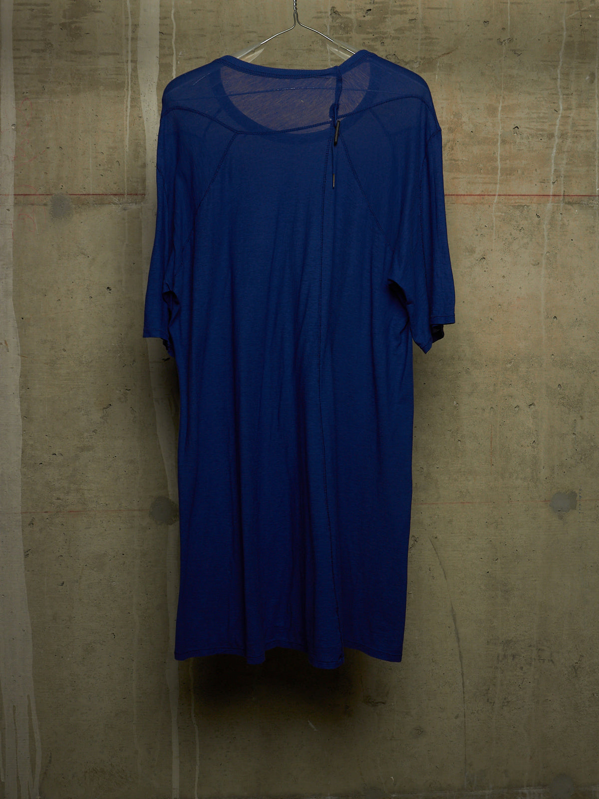 A royal blue short-sleeve dress hanging on a wire hanger against a textured concrete wall.