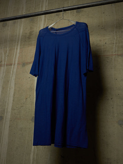 A royal blue short-sleeve dress hanging on a white hanger from a dark metal rod against a textured concrete wall.