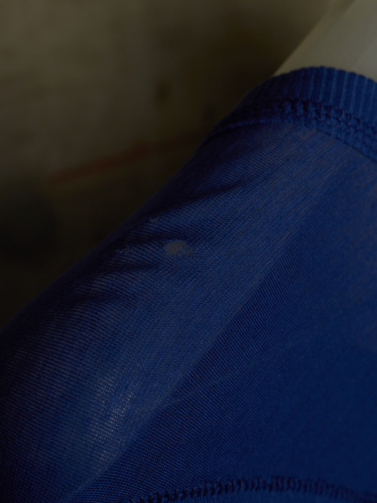 A close-up of a blue athletic jersey or t-shirt fabric, showing the textured knit material and ribbed collar stitching.