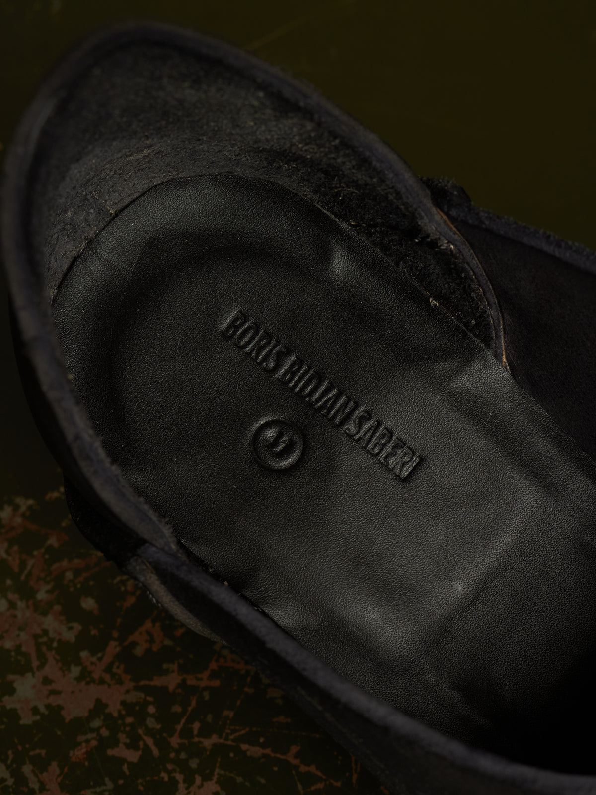 Close-up of the black suede and leather interior of a shoe, showing the embossed brand name BONES OF MAN SABERI.