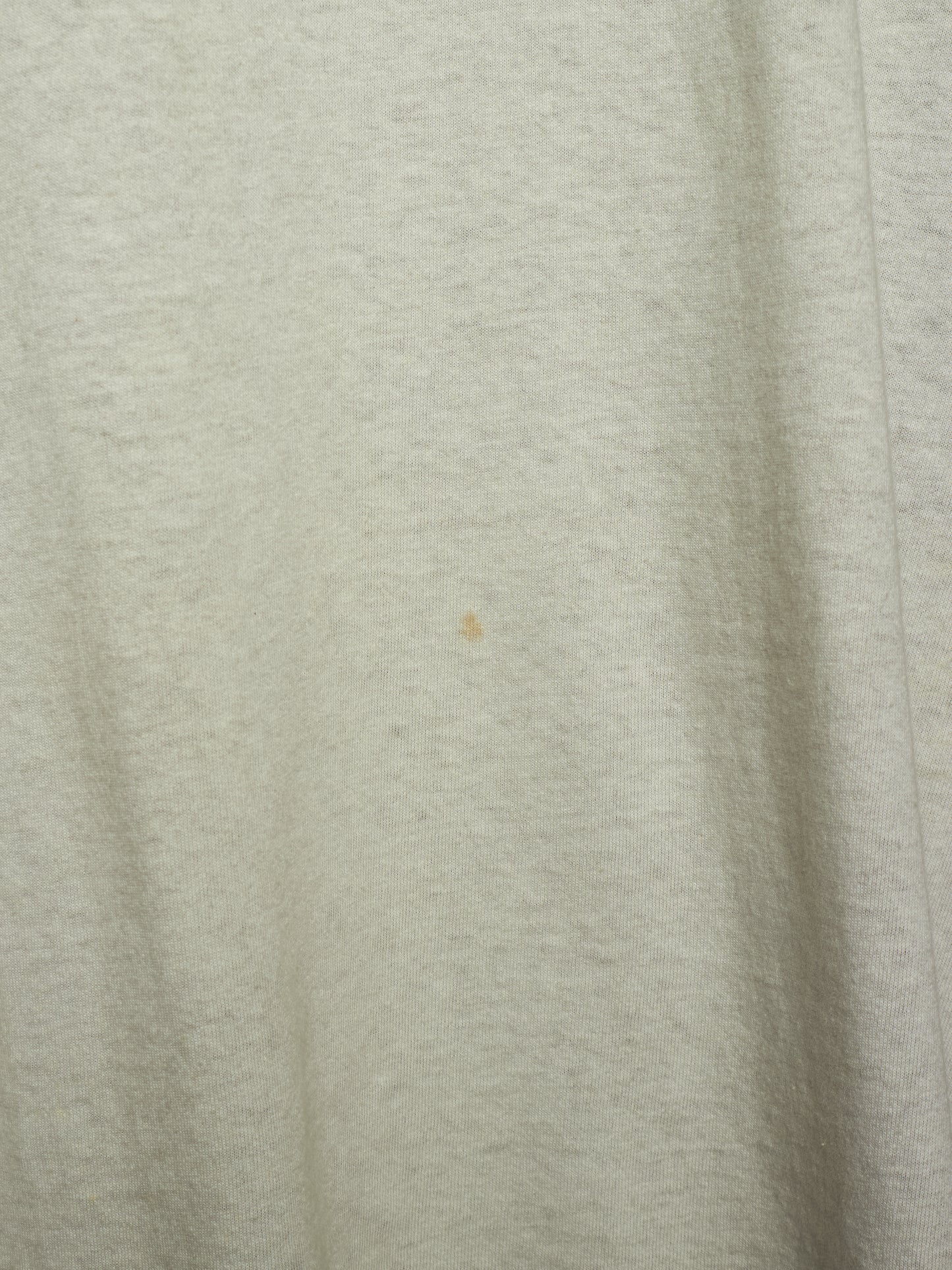 A close-up of a light heather gray fabric surface with soft folds and a tiny small brown speck near the center.