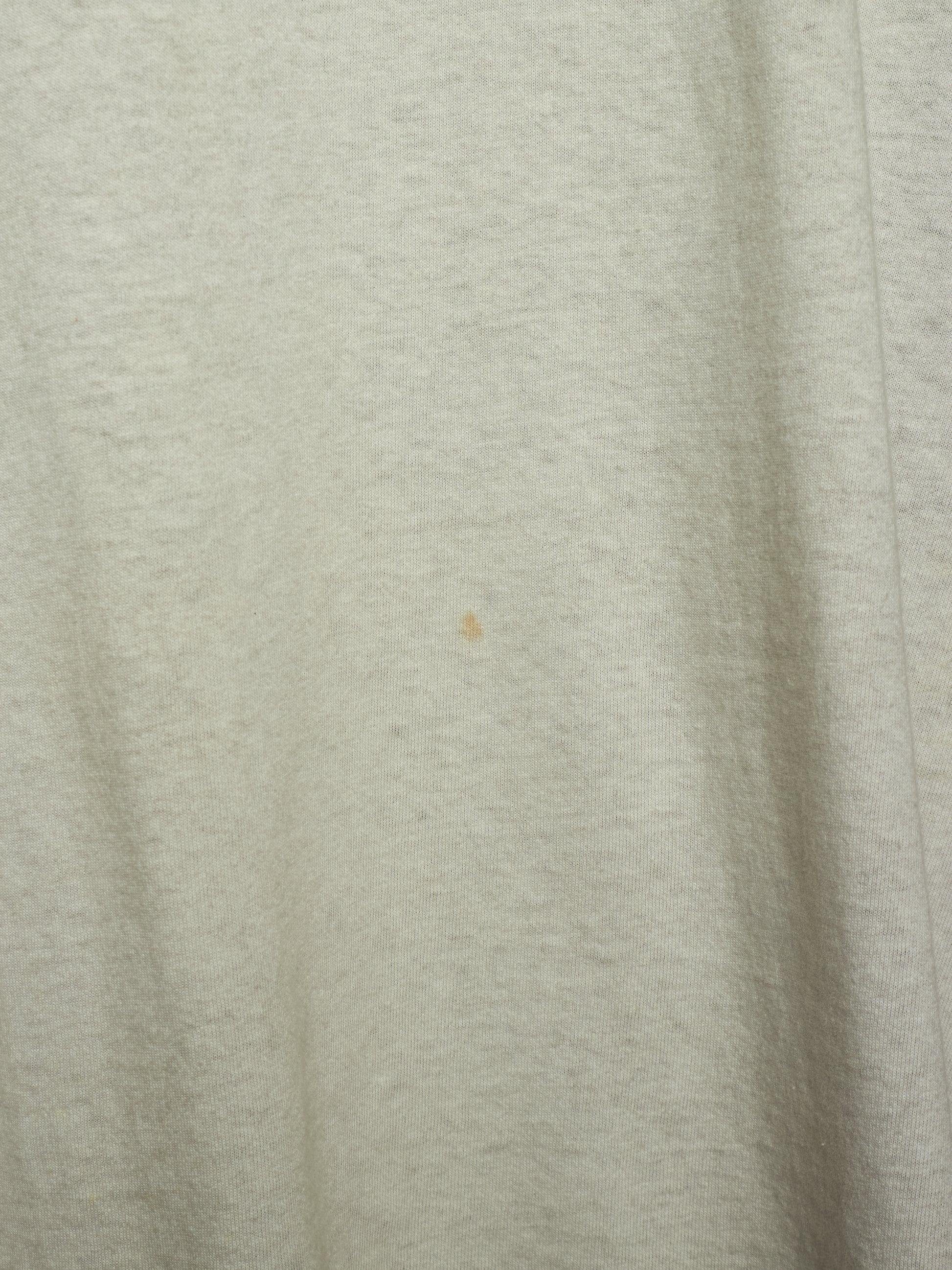 A close-up of a light heather gray fabric surface with soft folds and a tiny small brown speck near the center.